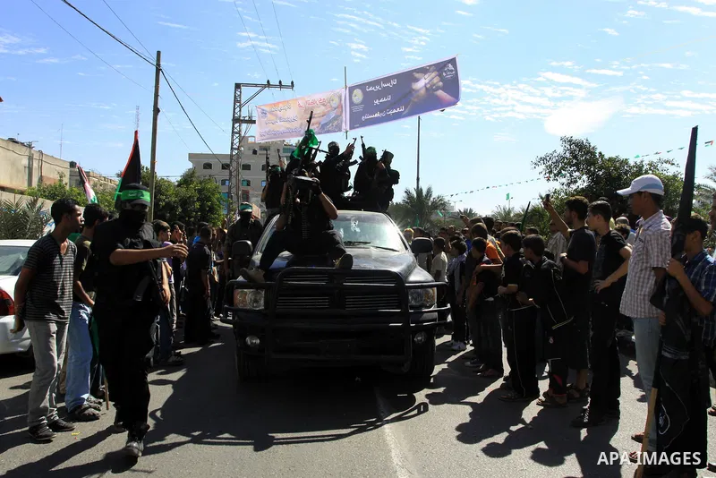 Palestinians keep watch as Hamas militants stand guard in Gaza City on October 18, 2011 as an Israeli-Palestinian prisoner swap deal gets under way. Captive Israeli soldier Gilad Shalit was today freed from five years of...