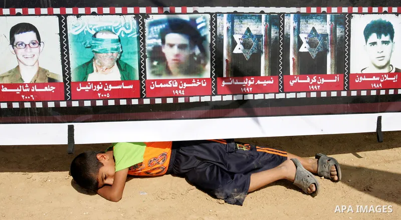 A Palestinian boy sleeps under a poster for Kidnaped Israeli soldiers by Palestinian militants laid at the reception tent of Hamas freed Palestinian prisoner Yehia Sinwar laid upon his return in the southern Gaza Strip t...