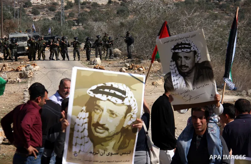 Palestinian protestors hold pictures of late leader Yasser Arafat in front of Israeli forces during a weekly demonstration against Israeli-occupation in the northern West Bank village of Kfar Kadum, on November 11, 2011....