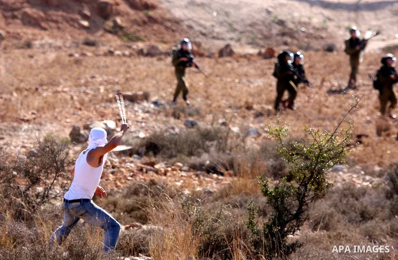 A Palestinian demonstrator uses a sling to hurl a stone towards Israeli soldiers during clashes between Israeli security forces and Palestinian demonstrators at a weekly protest in the West Bank village of Nabi Saleh, ne...