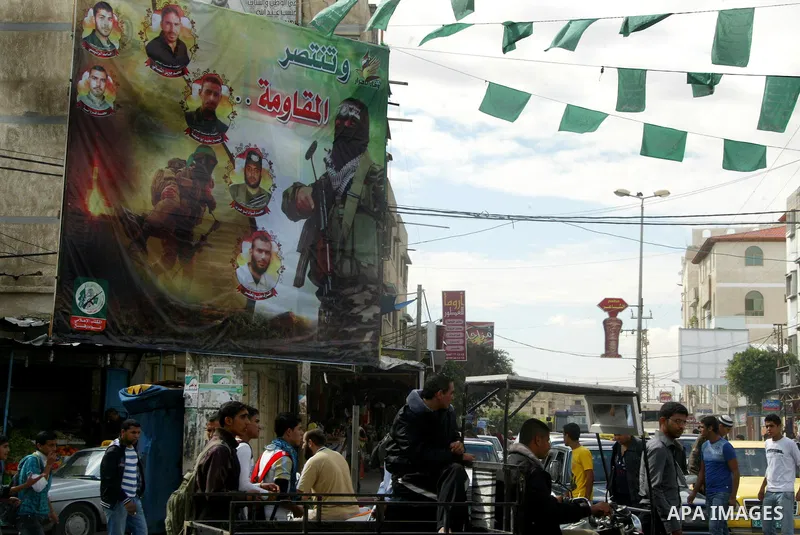 Palestinians walk next to a poster depicting members of Izz al-Din al-Qassam who killed by Israel, in the southern Gaza Strip town of Rafah on November 13, 2011. The Israeli army on Sunday maneuver and to repel a wide ab...