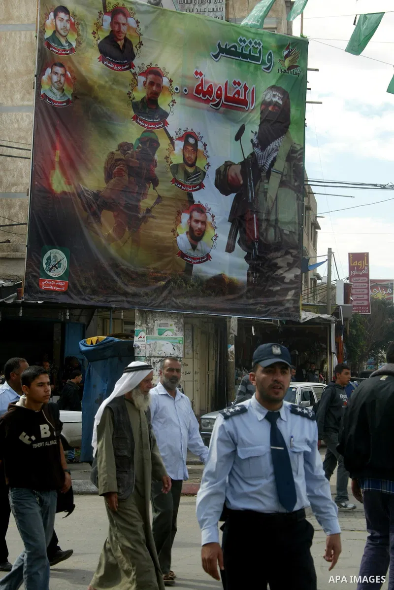 Palestinians walk next to a poster depicting members of Izz al-Din al-Qassam who killed by Israel, in the southern Gaza Strip town of Rafah on November 13, 2011. The Israeli army on Sunday maneuver and to repel a wide ab...