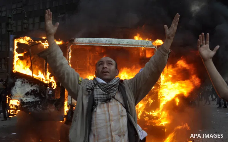 A protester stand next to a police vehicle that was set on fire during clashes between protesters and security forces at Tahrir Square in Cairo November 19, 2011. Clashes erupted between riot police and protesters in Cai...