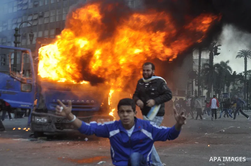 protesters stand next to a police vehicle that was set on fire during clashes between protesters and security forces at Tahrir Square in Cairo November 19, 2011. Clashes erupted between riot police and protesters in Cair...