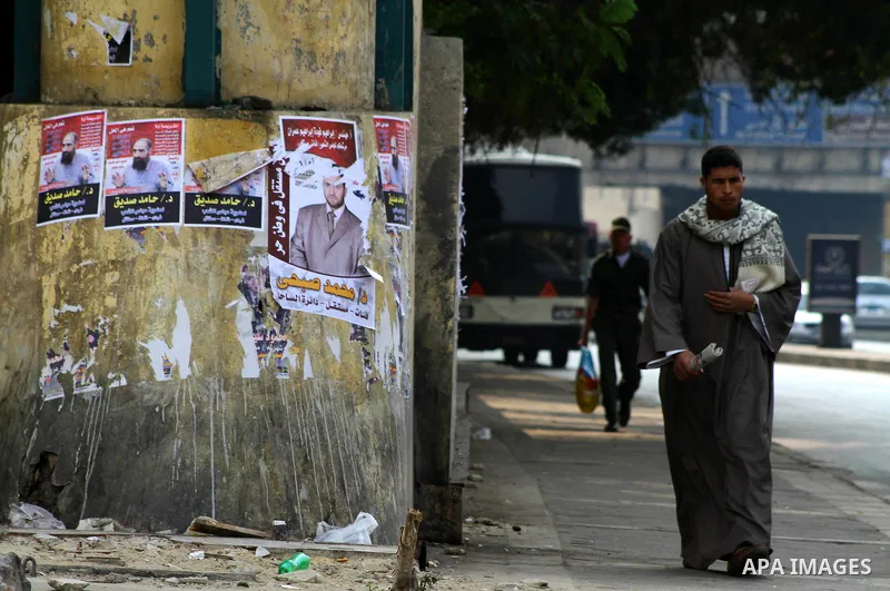 Egyptians walk past electoral campaign banners in Cairo on November 26, 2011 ahead of a three-round parliamentary election. The parliamentary elections that get underway on November 28 will be the first polls since a pop...