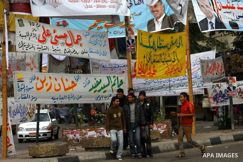 Egyptians walk past electoral campaign banners in Cairo on November 26, 2011 ahead of a three-round parliamentary election. The parliamentary elections that get underway on November 28 will be the first polls since a pop...