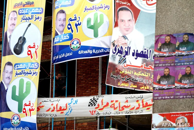 Egyptians walk past electoral campaign banners in Cairo on November 26, 2011 ahead of a three-round parliamentary election. The parliamentary elections that get underway on November 28 will be the first polls since a pop...