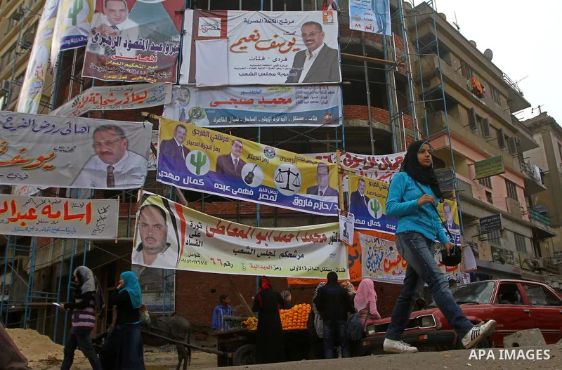 Egyptians walk past electoral campaign banners in Cairo on November 26, 2011 ahead of a three-round parliamentary election. The parliamentary elections that get underway on November 28 will be the first polls since a pop...