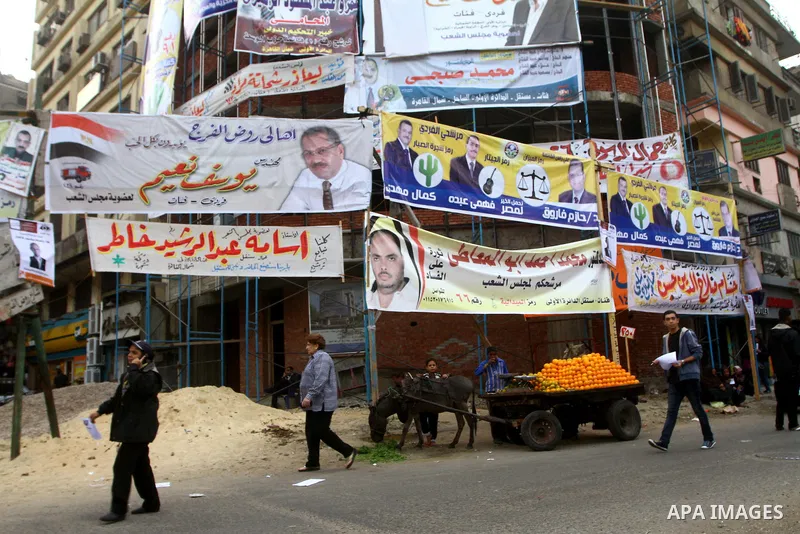 Egyptians walk past electoral campaign banners in Cairo on November 26, 2011 ahead of a three-round parliamentary election. The parliamentary elections that get underway on November 28 will be the first polls since a pop...