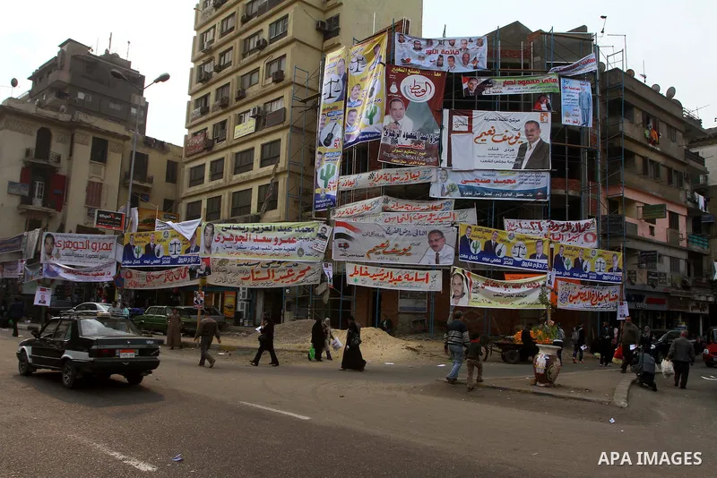 Egyptians walk past electoral campaign banners in Cairo on November 26, 2011 ahead of a three-round parliamentary election. The parliamentary elections that get underway on November 28 will be the first polls since a pop...