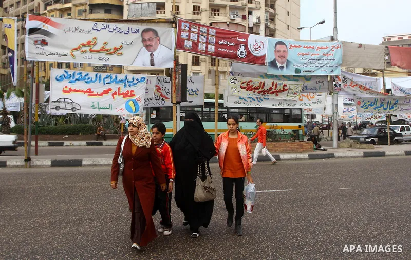 Egyptians walk past electoral campaign banners in Cairo on November 26, 2011 ahead of a three-round parliamentary election. The parliamentary elections that get underway on November 28 will be the first polls since a pop...