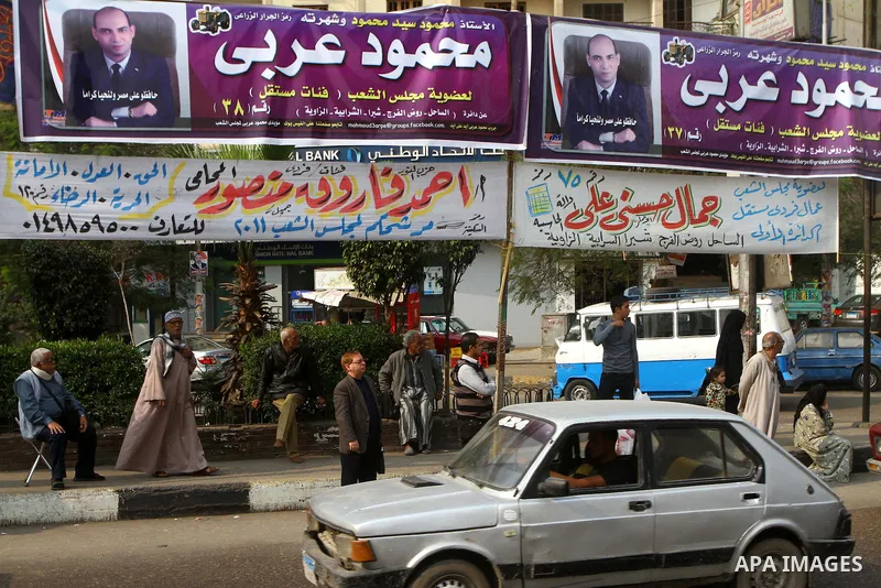 Egyptians walk past electoral campaign banners in Cairo on November 26, 2011 ahead of a three-round parliamentary election. The parliamentary elections that get underway on November 28 will be the first polls since a pop...