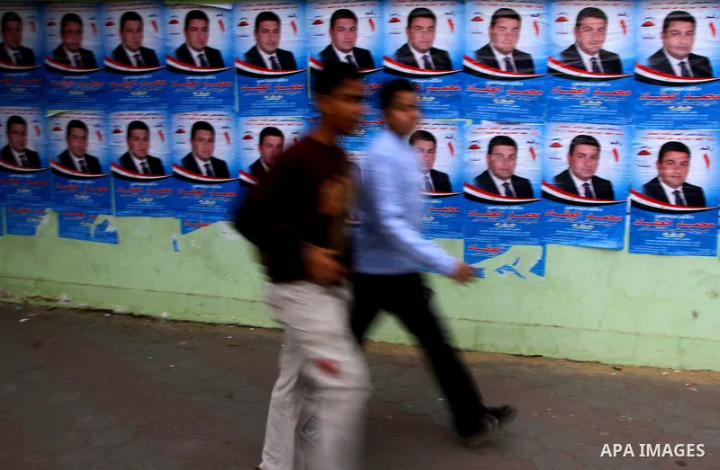 Egyptians walk past electoral campaign posters and banners for candidates in Cairo on November 27, 2011 on the eve of the first parliament elections since the end of the 30-year rule of strongman Hosni Mubarak. Photo by...