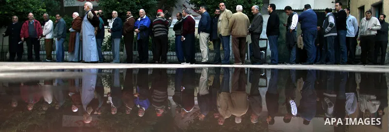 Voters line up outside a polling center beneath campaign posters on the first day of parliamentary elections in Cairo, Egypt, Monday, Nov. 28, 2011. Shaking off years of political apathy, Egyptians on Monday began voting...