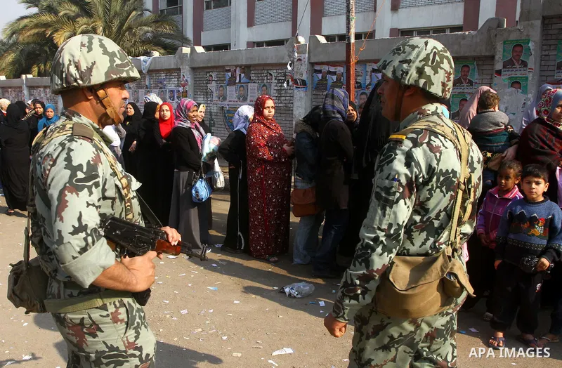 Army soldier stands guard as Egyptians wait in line to vote at a polling station in the Moqattam district of Cairo on November 29, 2011. Egypt hailed the start of its first post-revolution election as a triumph for democ...