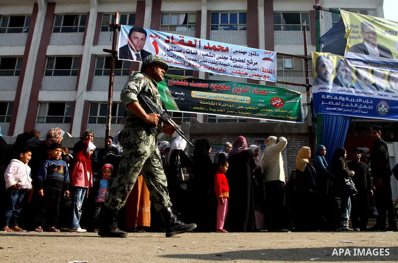 Army soldier stands guard as Egyptians wait in line to vote at a polling station in the Moqattam district of Cairo on November 29, 2011. Egypt hailed the start of its first post-revolution election as a triumph for democ...