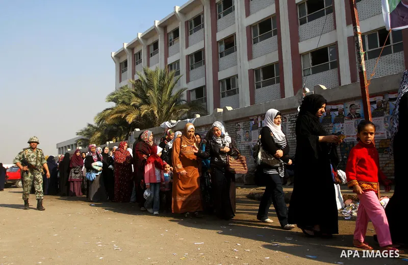 Army soldier stands guard as Egyptians wait in line to vote at a polling station in the Moqattam district of Cairo on November 29, 2011. Egypt hailed the start of its first post-revolution election as a triumph for democ...