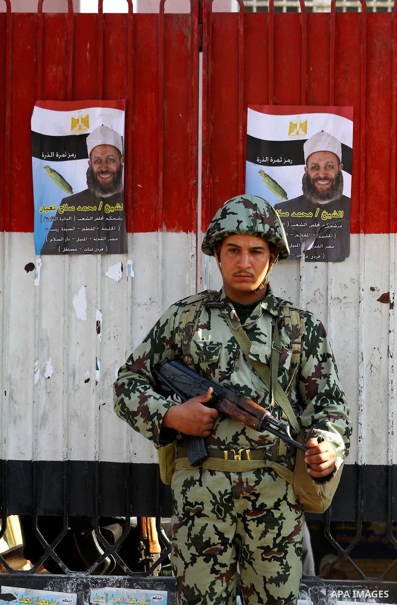 Army soldier stands guard as Egyptians wait in line to vote at a polling station in the Moqattam district of Cairo on November 29, 2011. Egypt hailed the start of its first post-revolution election as a triumph for democ...