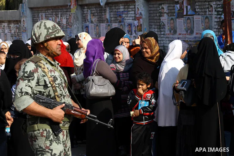 Army soldier stands guard as Egyptians wait in line to vote at a polling station in the Moqattam district of Cairo on November 29, 2011. Egypt hailed the start of its first post-revolution election as a triumph for democ...