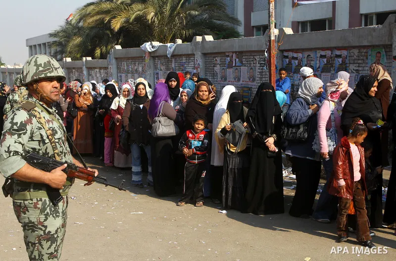 Army soldier stands guard as Egyptians wait in line to vote at a polling station in the Moqattam district of Cairo on November 29, 2011. Egypt hailed the start of its first post-revolution election as a triumph for democ...