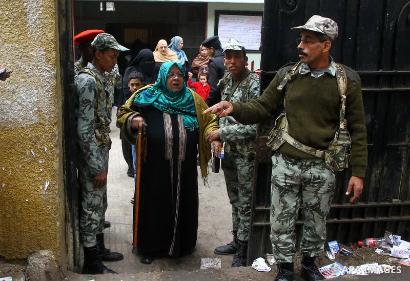 Army soldier helps an Egyptian woman to cast her ballot at a parliamentary polling station in Cairo on November 29, 2011. Egypt hailed the start of its first post-revolution election as a triumph for democracy as more vo...