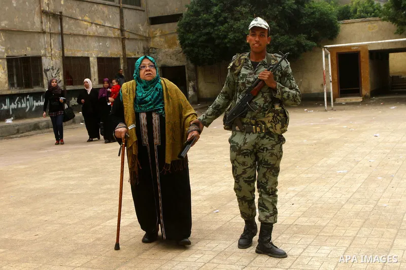 Army soldier helps an Egyptian woman to cast her ballot at a parliamentary polling station in Cairo on November 29, 2011. Egypt hailed the start of its first post-revolution election as a triumph for democracy as more vo...