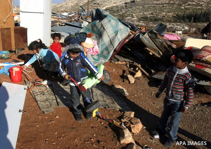 Palestinian Bedouin children collect belongings amidst the rubble of a structure after it was razed by the Israeli army in the West Bank village of Zayem, near Jerusalem November 29, 2011. According to Israeli authoritie...