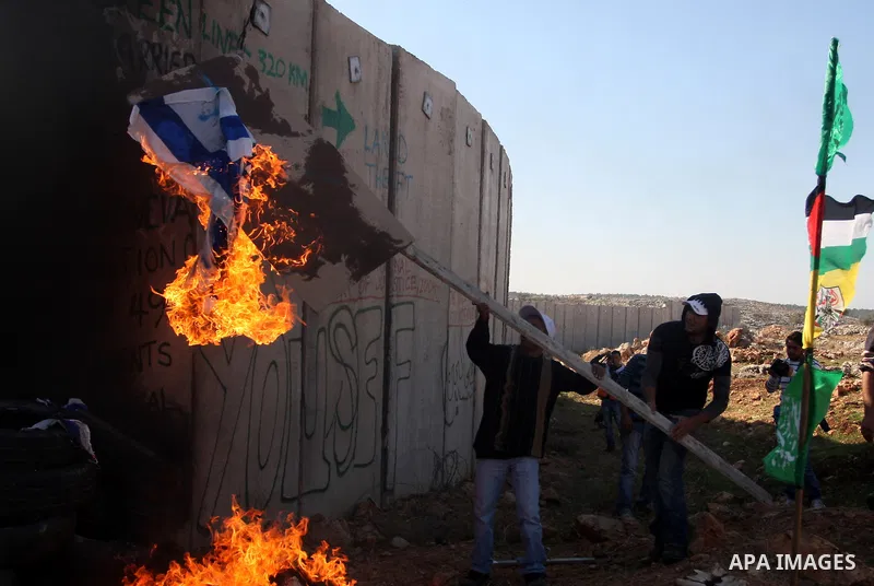 Palestinian protestors set fire the US and Israeli flags during a weekly demonstration near Israel's separation wall in the West Bank village of Nilin, on December 02, 2011. Photo by Issam Rimawi