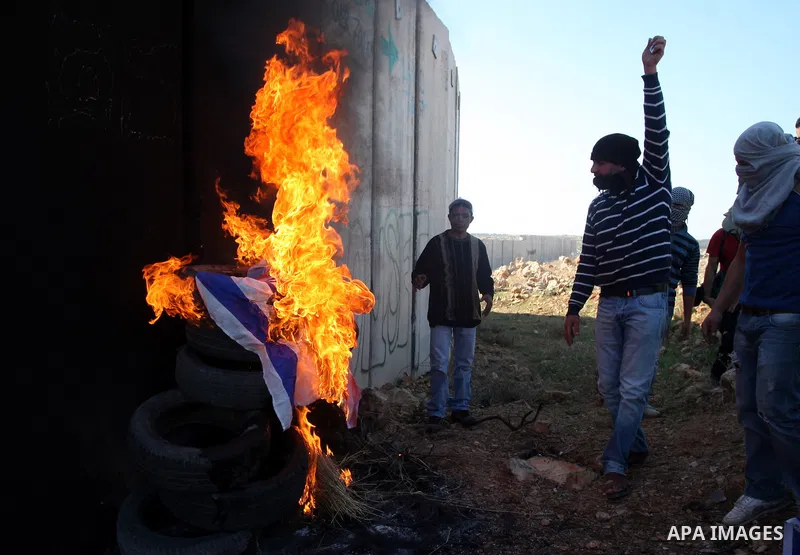 Palestinian protestors set fire the US and Israeli flags during a weekly demonstration near Israel's separation wall in the West Bank village of Nilin, on December 02, 2011. Photo by Issam Rimawi