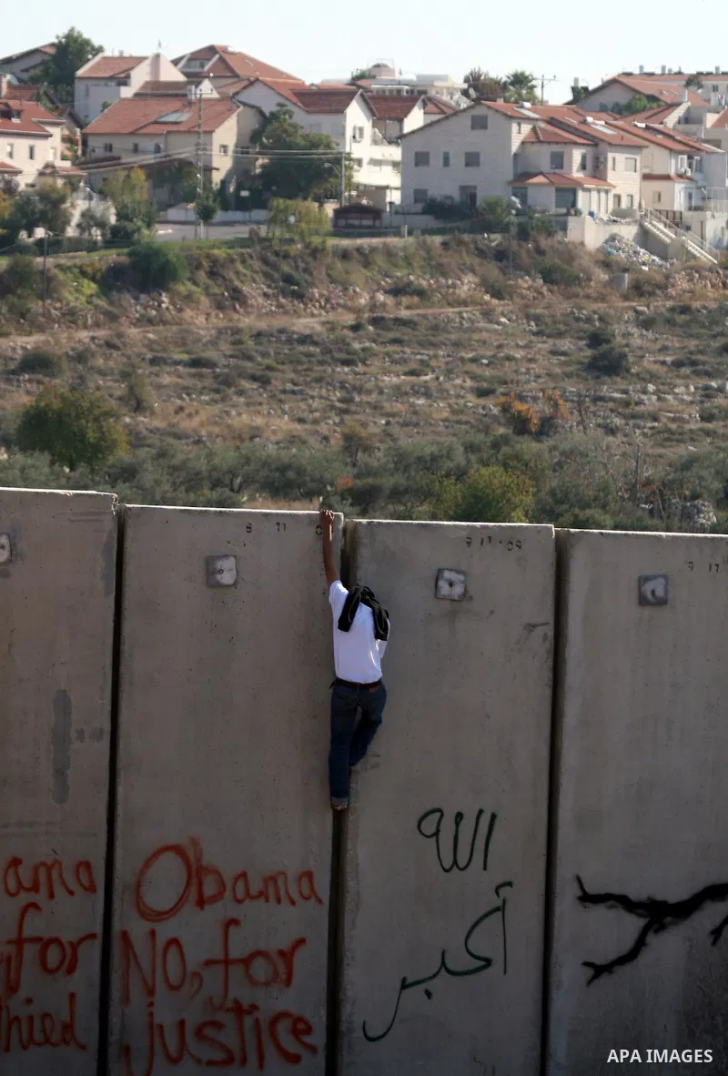 A masked Palestinian protestor climbs Israel's separation wall during a weekly demonstration against Israeli occupation in the West Bank village of Nilin, on December 02, 2011. Photo by Issam Rimawi