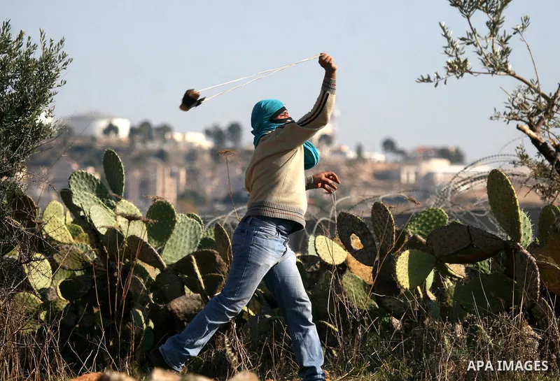 Palestinian protestors clash with Israeli forces standing on the other side of Israel's separation wall during a weekly protest in the West Bank village of Nilin, on December 02, 2011. Photo by Issam Rimawi