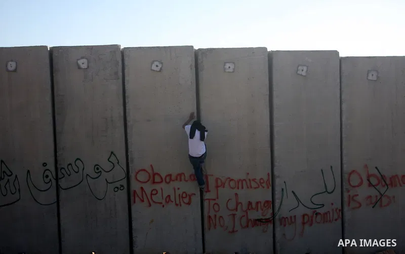 A masked Palestinian protestor climbs Israel's separation wall during a weekly demonstration against Israeli occupation in the West Bank village of Nilin, on December 02, 2011. Photo by Issam Rimawi