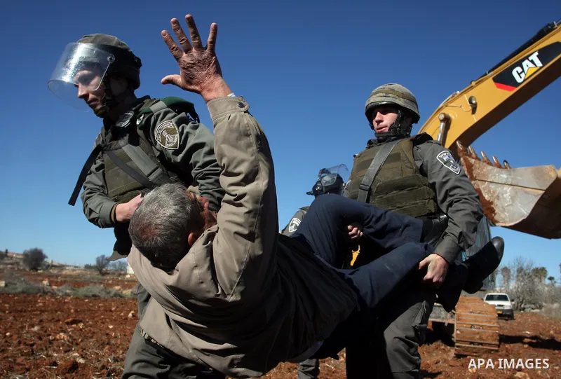 A Palestinian man is carried by Israeli border police officers after he tried to block a construction vehicle from working on Israel's barrier in the West Bank village of Qaladiya near Ramallah December 4, 2011. Accordin...
