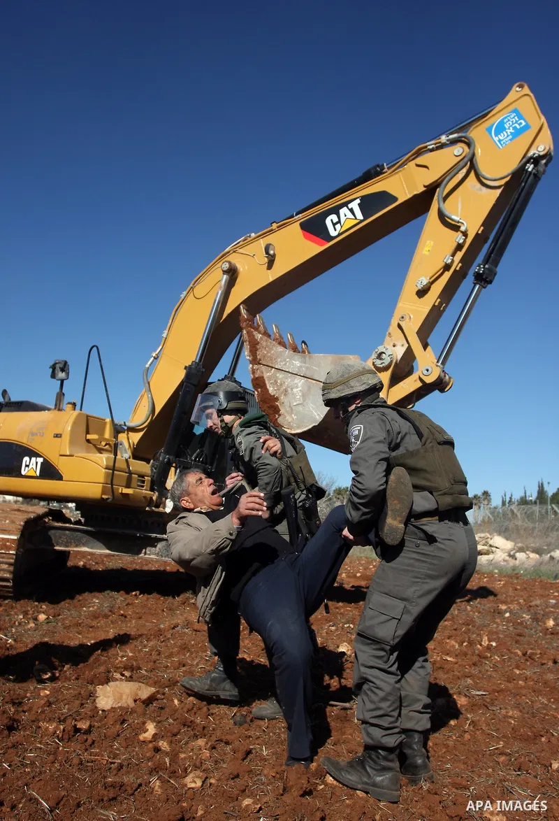 A Palestinian man is carried by Israeli border police officers after he tried to block a construction vehicle from working on Israel's barrier in the West Bank village of Qaladiya near Ramallah December 4, 2011. Accordin...