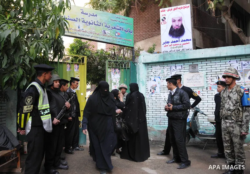 People walk past police and soldiers guarding the entrance to a polling station in the run-off of the first round of voting in the Cairo neighbourhood of Bab El-Shaeria on December 5, 2011. Islamist candidates in Egypt l...