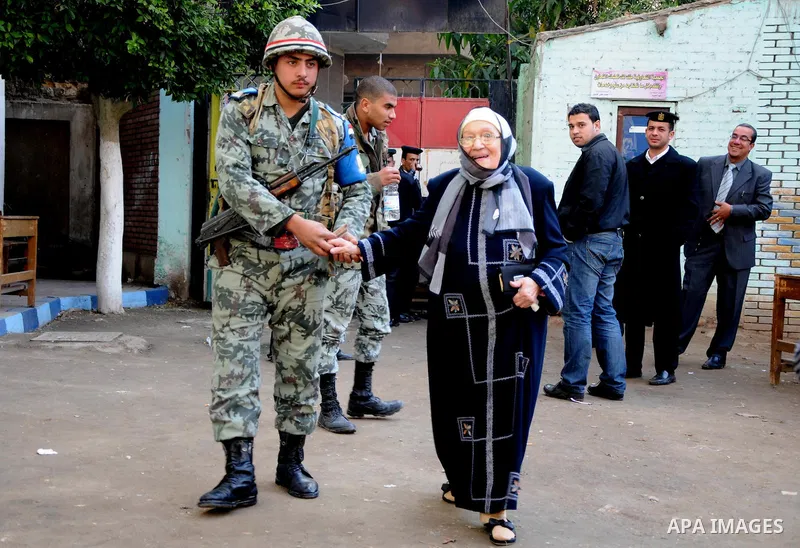 People walk past police and soldiers guarding the entrance to a polling station in the run-off of the first round of voting in the Cairo neighbourhood of Bab El-Shaeria on December 5, 2011. Islamist candidates in Egypt l...