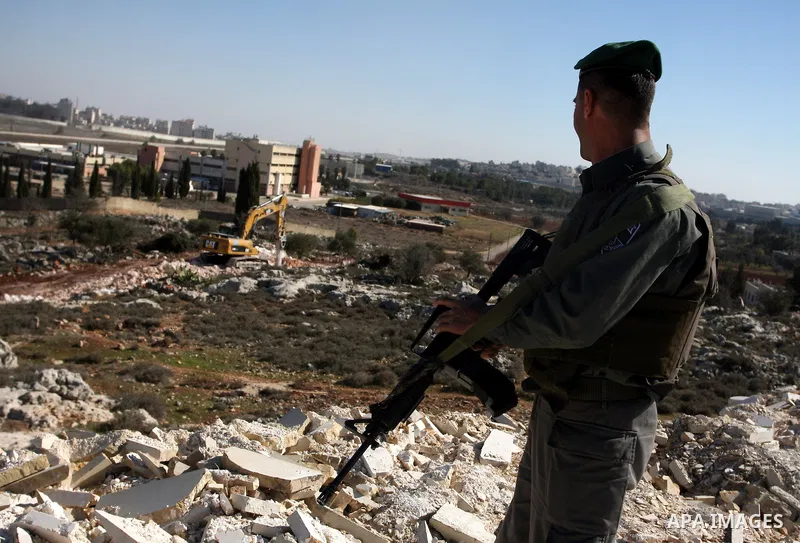 An Israeli border police officer stands guar as a vehicle work on Israel's barrier in the West Bank village of Qalandiya near Ramallah December 7, 2011. According to a witness, about 20 residents of the village protested...