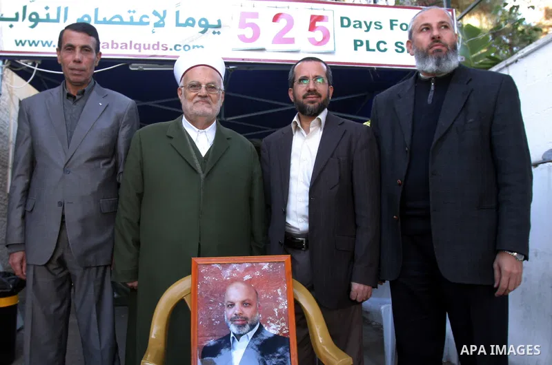 Palestinian Hamas lawmakers Mohammed Totah and Khaled Abu Arafa hold a picture for Hamas lawmaker Ahmed Abu Attoun at Red Cross headquarters in east Jerusalem on Dec. 6,2011. Israel has expelled a Hamas lawmaker who was...
