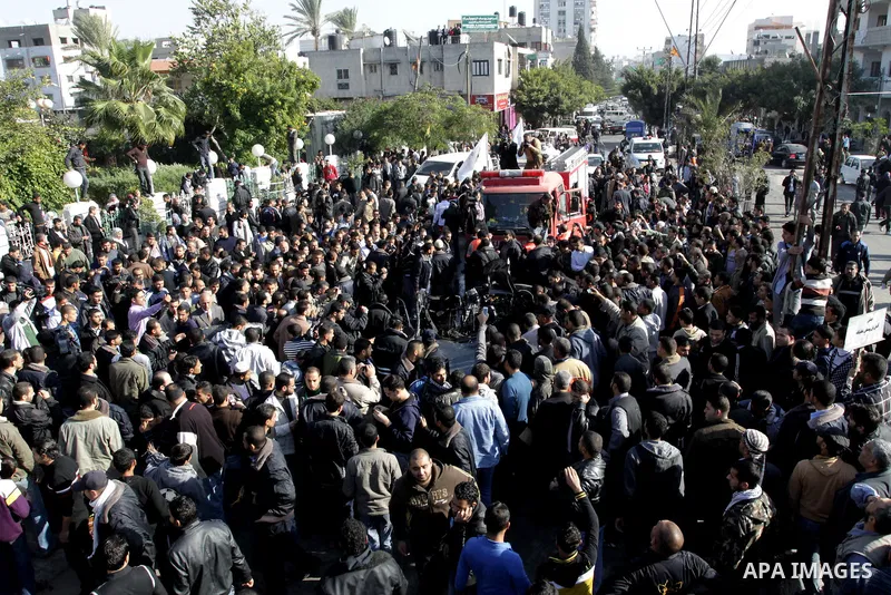 Palestinians crowd around the remains of a car hit by an Israeli air strike in Gaza City December 8, 2011. An Israeli air strike on the car killed at least two Hamas militants and wounded two others on a crowded Gaza str...