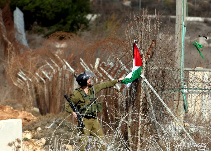 An Israeli soldier takes down a Palestinian flag during a protest against the construction of Israel's separation barrier in the West Bank village of Qalandia, near Ramallah, on December 9, 2011. Photo by Issam Rimawi