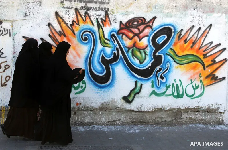 Palestinians walk past a mural depicting slogans for Hamas in the preparation of the anniversary of Hamas Islamic movement foundation in Rafah refugee camp, in southern Gaza Strip on December 11, 2011. Photo by Hatem Oma...