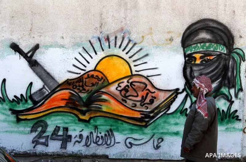 Palestinians walk past a mural depicting slogans for Hamas in the preparation of the anniversary of Hamas Islamic movement foundation in Rafah refugee camp, in southern Gaza Strip on December 11, 2011. Photo by Hatem Oma...