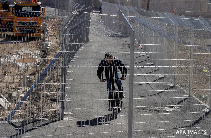 Israeli soldiers stand guard as Palestinians cross through the new opened Israeli checkpoint near the east Jerusalem refugee camp of Shuafat on December 12, 2011. Palestinian youths protested against the construction of...