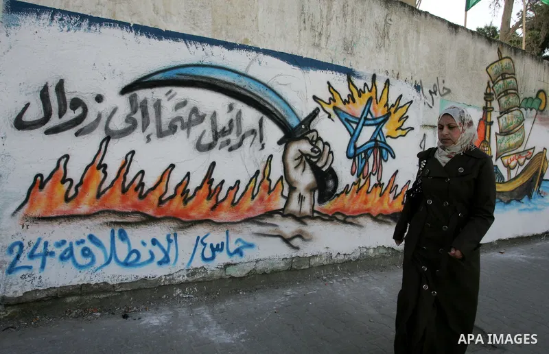 Palestinians walk past murals depicting slogans for Hamas in preparation for the celebrations marking the Islamist movement's 24th anniversary, Rafah refugee camp, in southern Gaza Strip on Dec. 13,2011. The main celebra...