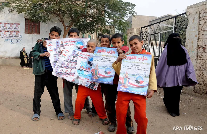 A boys hold pictures slogans for Salafi political party Al-Nour that reads: "Together to win", outside a polling station during a second round of voting in parliamentary elections, at a village in Beheira, 135 km (83 mil...