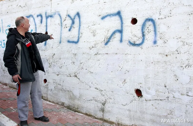 A Palestinian man stand next a graffiti in Hebrew which residents said was written by Jewish settlers in the West Bank Village of Harith near Nablus, Wednesday , Dec. 12, 2011. leaving behind a graffiti message in Hebrew...