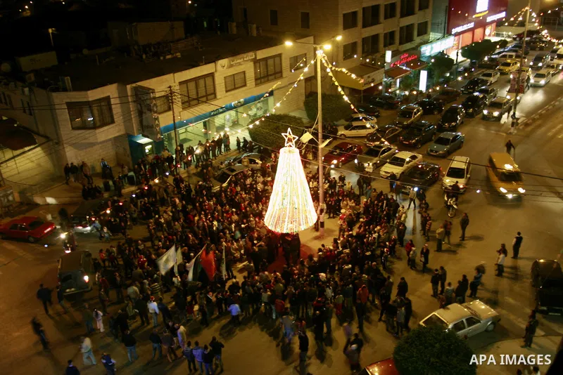 Palestinians watch the lighting of a Christmas tree outside the Church in West Bank town of Nablus Monday, Dec. 19, 2011. Christian worshipers began their spiritual preparations ahead of Christmas Eve and tourists from a...