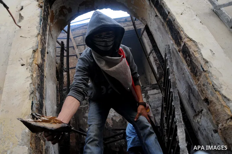 Smokes rises as an Egyptian protester helps extinguish smoldering valuable books and documents salvaged from the two story building of the Egyptian Scientific Complex after it was almost gutted by fire which broke out du...