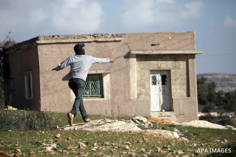A Palestinian youth uses a sling to throw a stone toward Israeli soldiers during clashes at a weekly protest in the West Bank village of Nabi Saleh, near Ramallah, December 23, 2011.