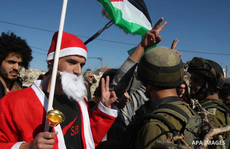 An Israeli soldier pushes back a demonstrator dressed as Santa Claus and holding a Palestinian flag during a protest against the controversial Israeli barrier in the West Bank village of al-Masara near Bethlehem December...